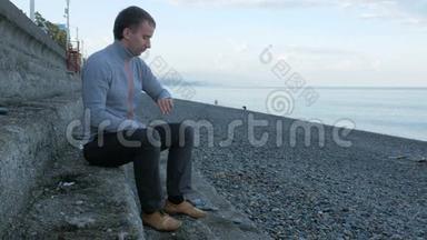 一<strong>个人</strong>坐在靠近海洋卵石海滩的台阶上。 它扫描智能手表上的<strong>信息</strong>并回应社交